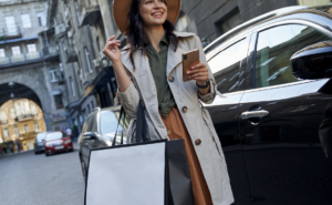 A happy woman with shopping bags beside a luxury service vehicle, exemplifying the convenience of chauffeurs London for personalized shopping trips.
